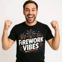 A person with a beard is smiling widely and raising their fists in excitement. They are wearing a black t-shirt with colorful firework designs around the text 