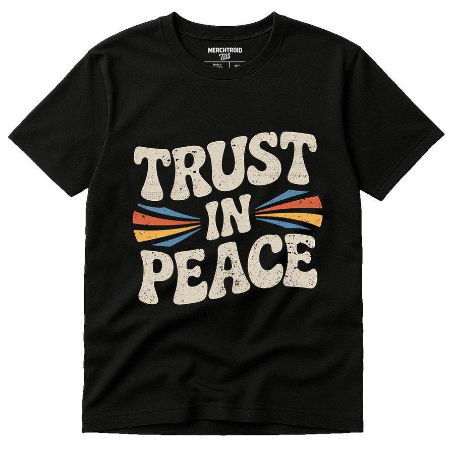 A black t-shirt with bold, retro-style text that reads "TRUST IN PEACE" in cream-colored letters. The design includes colorful arrows pointing inward toward the word "IN." The shirt has a round neckline and short sleeves.