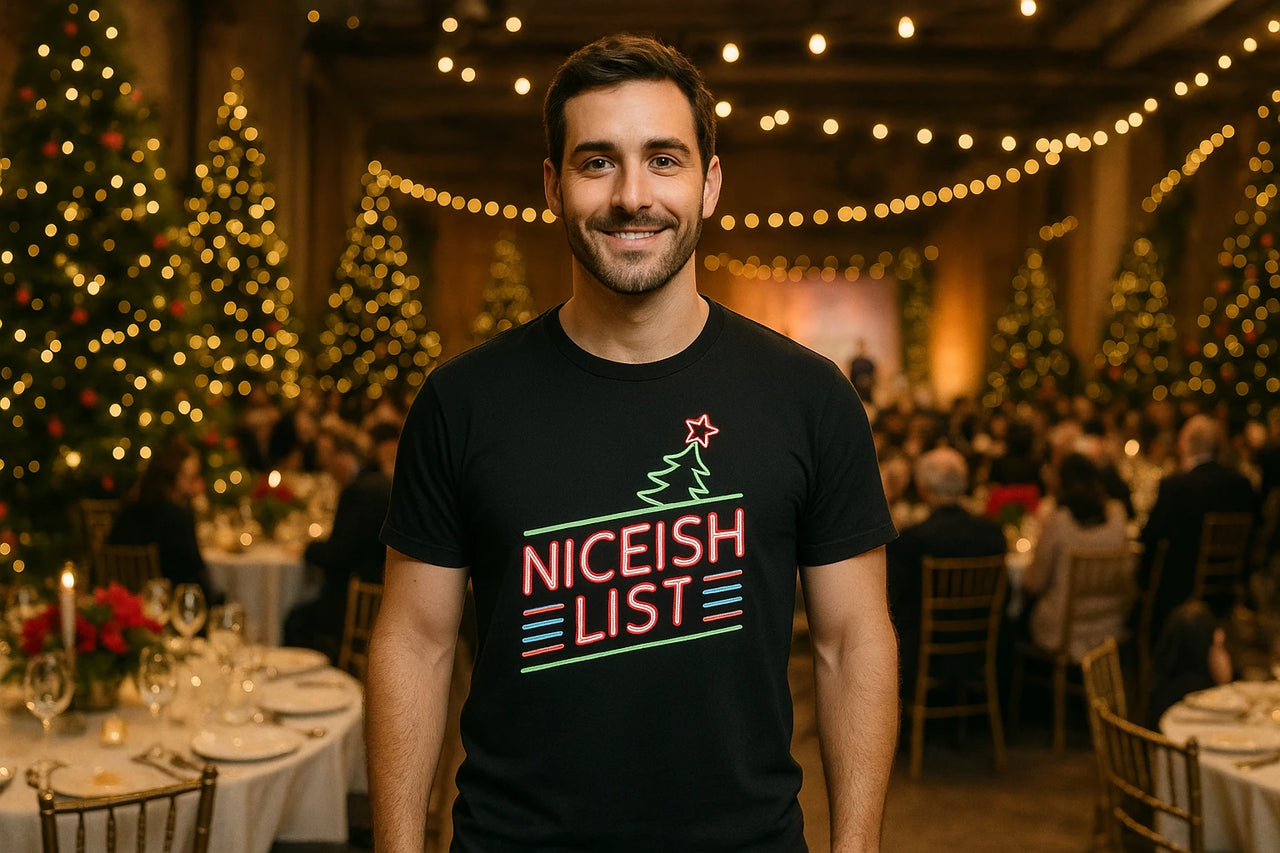 A person stands in a festive, warmly lit venue with decorated Christmas trees and dining tables in the background. They are wearing a black shirt with neon-style text and a Christmas tree graphic.