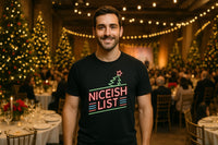 A person stands in a festive, warmly lit venue with decorated Christmas trees and dining tables in the background. They are wearing a black shirt with neon-style text and a Christmas tree graphic.
