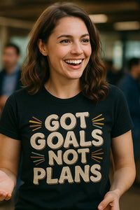 A person with shoulder-length brown hair is smiling and wearing a black t-shirt with the text 