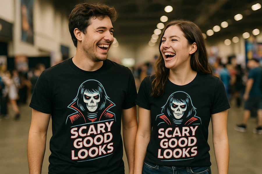 A man and a woman standing side by side, both laughing and wearing matching black T-shirts with a graphic of a skeleton face and the text "SCARY GOOD LOOKS." They are in a large, indoor space with people in the background.