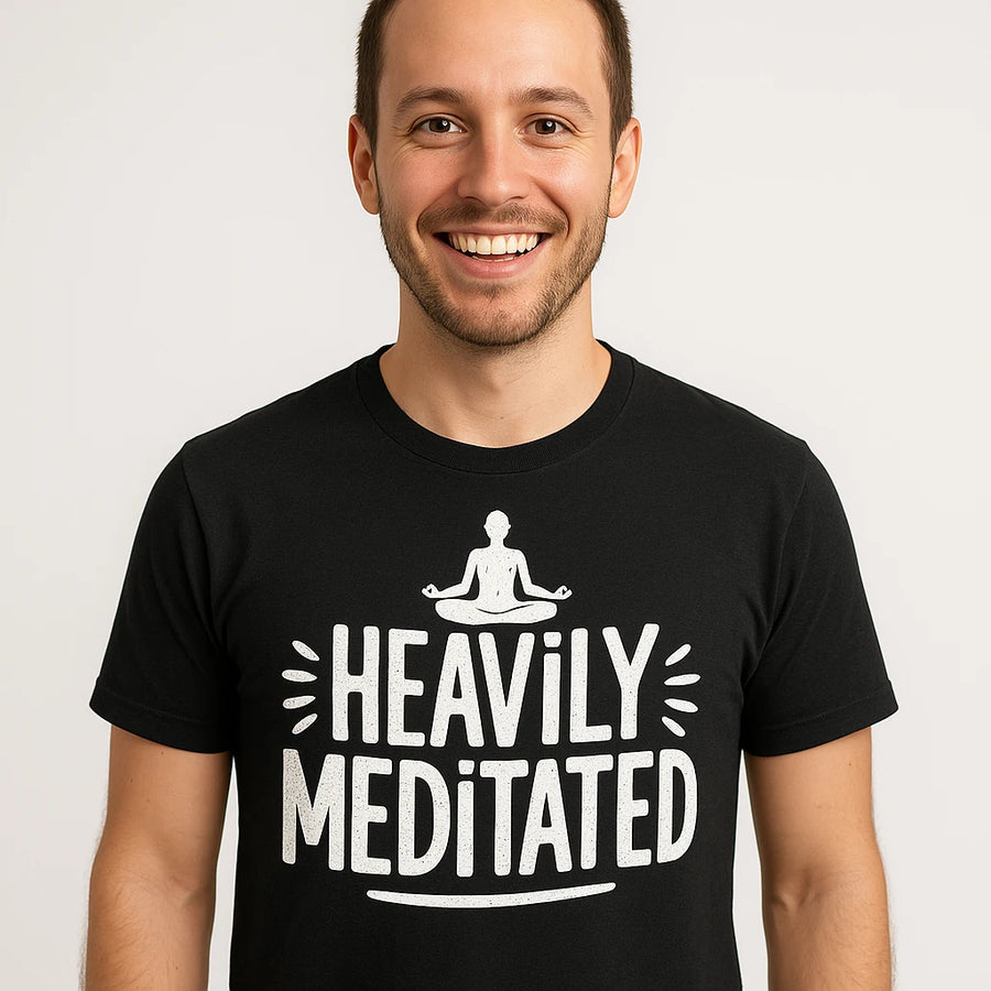 A smiling person wearing a black T-shirt with the text "HEAVILY MEDITATED" and an illustration of a meditating figure. The background is plain white.