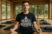 A person sits cross-legged in a meditation pose inside a serene room with large windows. They are wearing a black T-shirt with a design of a meditating figure above the words 