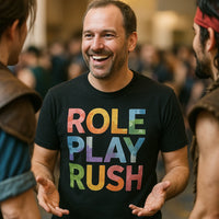 A man with short hair and a beard is smiling and engaging in conversation. He is wearing a black t-shirt with colorful text that reads 
