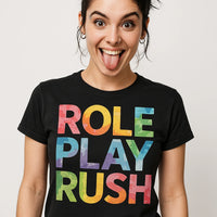 A person with dark hair styled up, wearing hoop earrings and a stud eyebrow piercing, is sticking their tongue out playfully. They are wearing a black T-shirt with multicolored text.