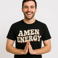 A person with short dark hair and a beard is smiling and standing against a plain background. They are wearing a black T-shirt with the words 
