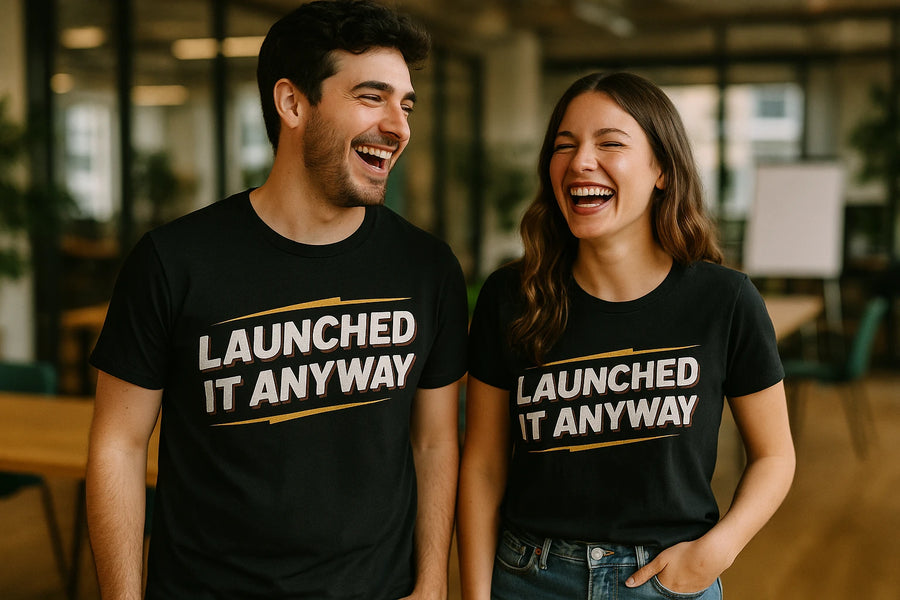 A man and a woman standing next to each other, both smiling and wearing black T-shirts with the text "LAUNCHED IT ANYWAY" printed on them. They are in an indoor setting with a blurred background, suggesting a casual, possibly office-like environment. The woman has long wavy hair, and both appear to be enjoying a cheerful moment.