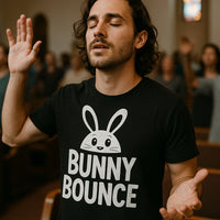 A person with long hair and a beard, wearing a black t-shirt with a cartoon bunny graphic and the text 