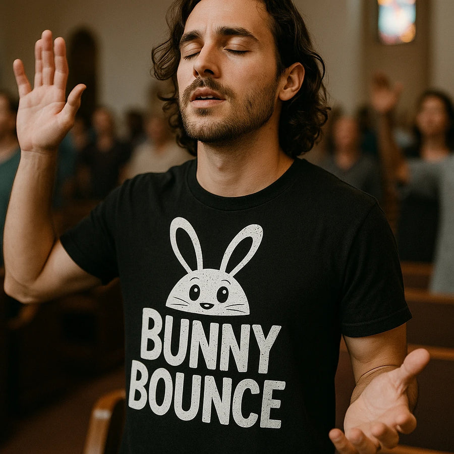 A person with long hair and a beard, wearing a black t-shirt with a cartoon bunny graphic and the text "BUNNY BOUNCE." The person has their eyes closed and hands raised, standing indoors among other people with similar posture.