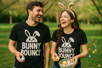 A man and a woman stand laughing in a park, both wearing black T-shirts with a bunny graphic and the text 