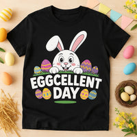 A black T-shirt featuring a cartoon bunny with pink ears peeking over grass, surrounded by colorful Easter eggs. The phrase 