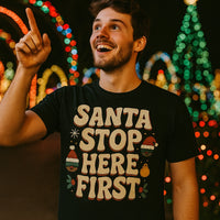 A cheerful person with short hair and a beard is pointing upwards and smiling. The person is wearing a black shirt with festive lights in the background, celebrating a holiday atmosphere.