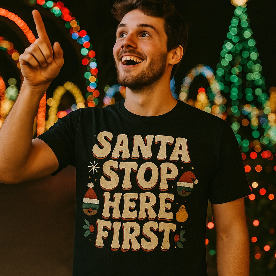 A cheerful person with short hair and a beard is pointing upwards and smiling. The person is wearing a black shirt with festive lights in the background, celebrating a holiday atmosphere.