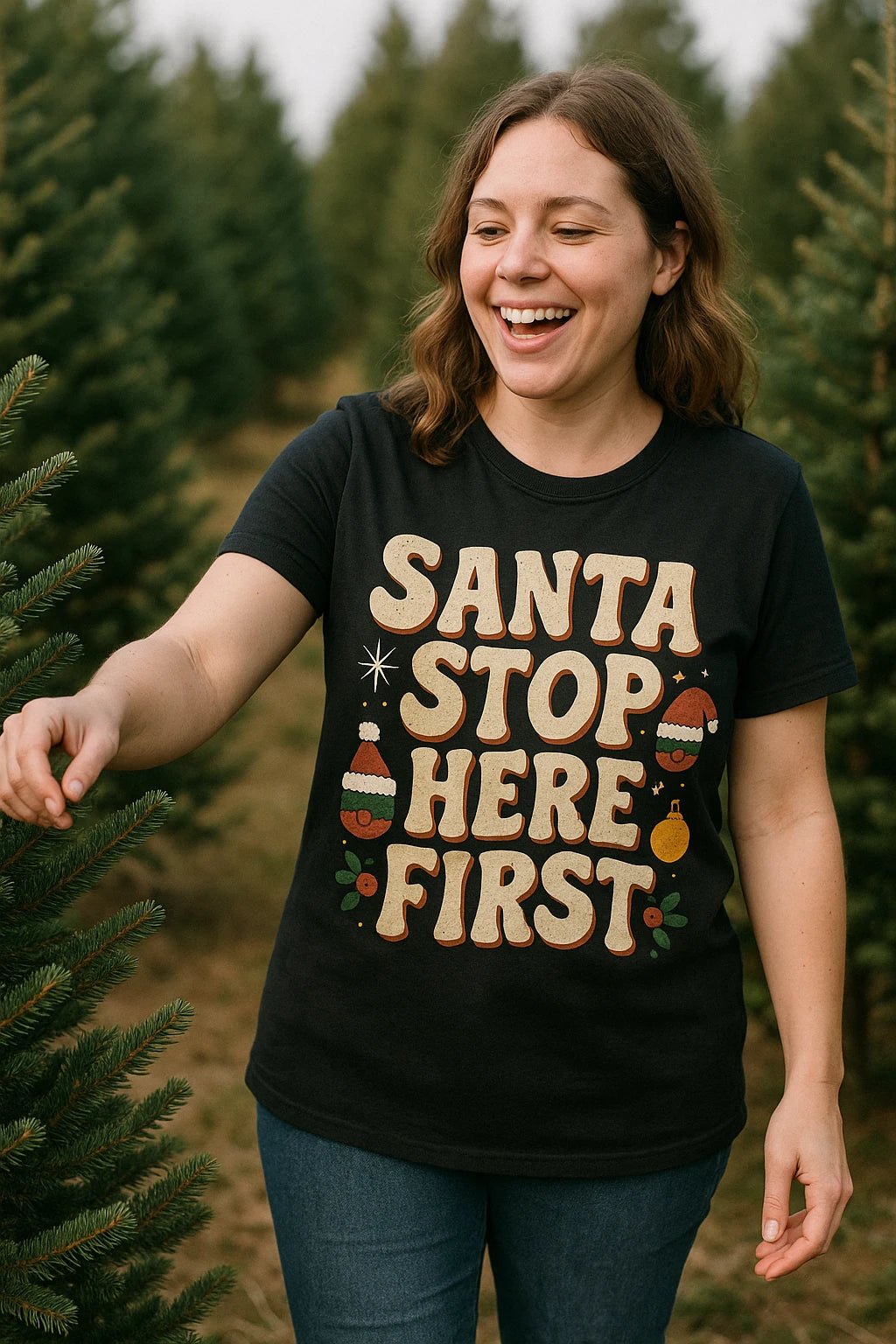 A person with shoulder-length brown hair is smiling and standing among evergreen trees. They are wearing a black T-shirt with festive decorations and playful text. The background shows a Christmas tree farm setting.