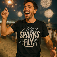 A person is joyfully holding a sparkler at a celebration with fireworks in the night sky. They are wearing a black shirt that reads 