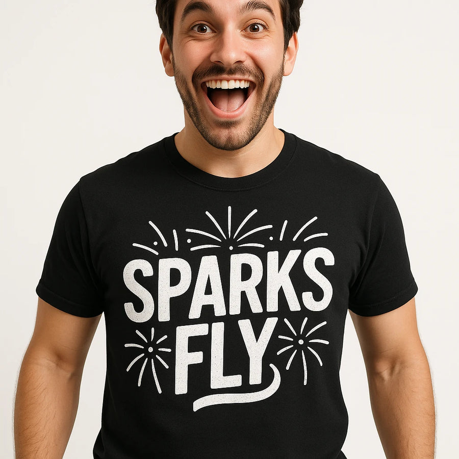 A person with dark hair and facial hair is wearing a black t-shirt with the words "SPARKS FLY" in bold white letters, with decorative spark designs around the text. The person has an open-mouthed smile and appears excited.