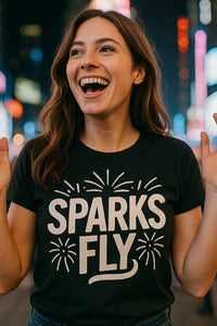 A person with long brown hair is smiling widely, wearing a black t-shirt with the text 