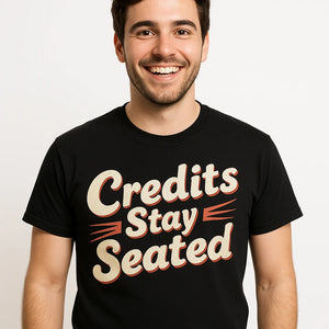 Close-up of the "Credits Stay Seated" beige print on a premium Bella+Canvas black graphic tee