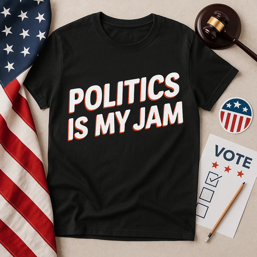 A black t-shirt with the text "POLITICS IS MY JAM" in bold white and red letters is laid on a flat surface. Next to it are a gavel, a pencil, a sheet with the word "VOTE" and checkboxes, a circular sticker with stars and stripes, and an American flag.