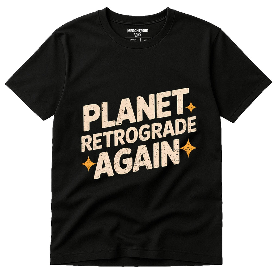 A black t-shirt with bold cream-colored text that reads "PLANET RETROGRADE AGAIN," featuring two small orange star graphics.