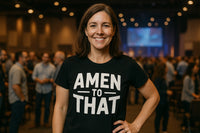 A person with shoulder-length brown hair is smiling and wearing a black T-shirt with the text 