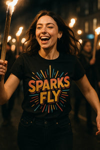 A person is joyfully holding a torch in a nighttime setting, wearing a black T-shirt with colorful lettering that reads 