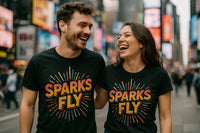 A man and a woman are standing close together in a lively urban setting, both wearing matching black t-shirts with colorful lettering that reads 