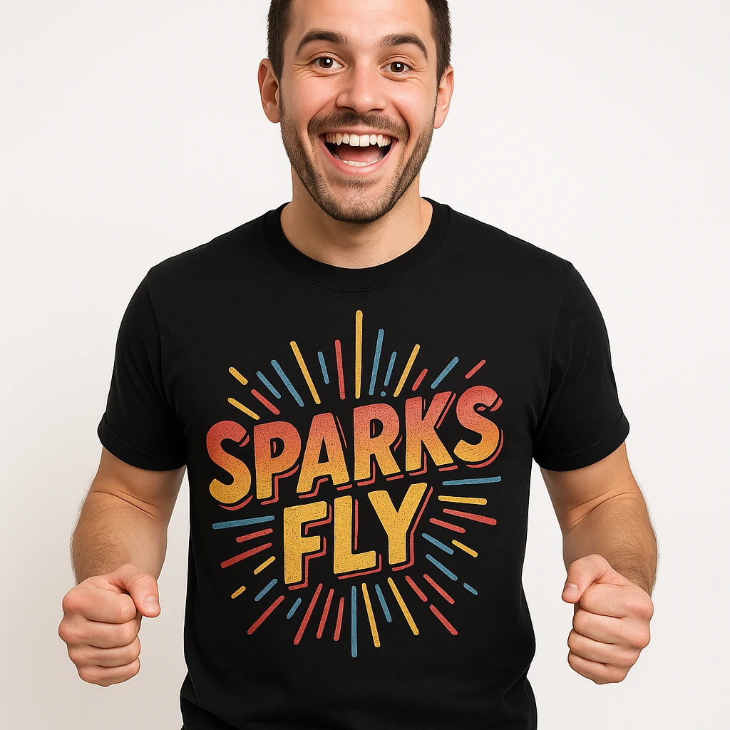 A person wearing a black t-shirt with colorful text that reads "SPARKS FLY." They have a cheerful expression, smiling widely, with short hair and are standing against a plain background.