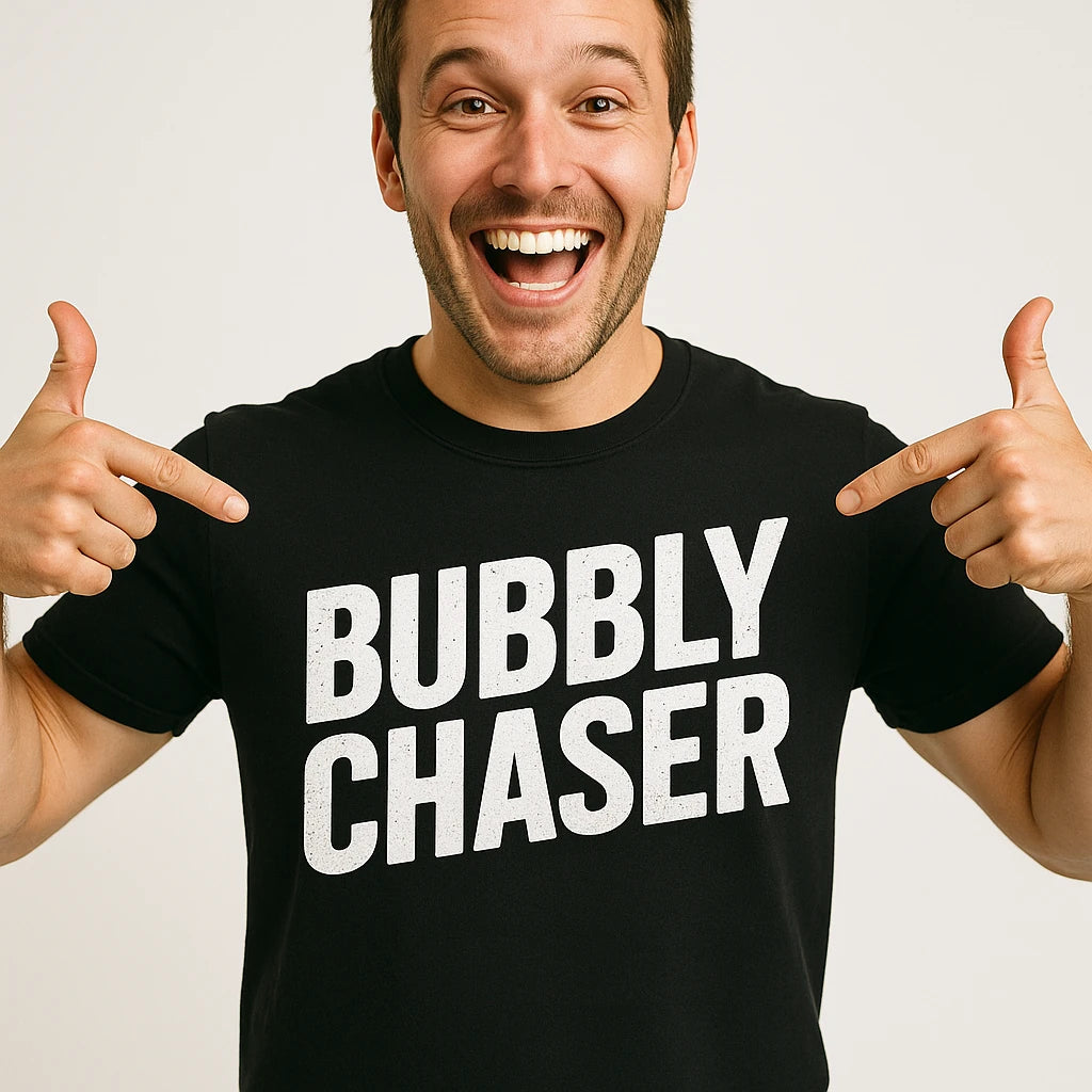A person wearing a black t-shirt with the words "BUBBLY CHASER" in large white letters. They are smiling widely and pointing at the text on the shirt. The background is plain white.