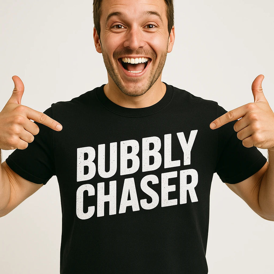 A person wearing a black t-shirt with the words "BUBBLY CHASER" in large white letters. They are smiling widely and pointing at the text on the shirt. The background is plain white.