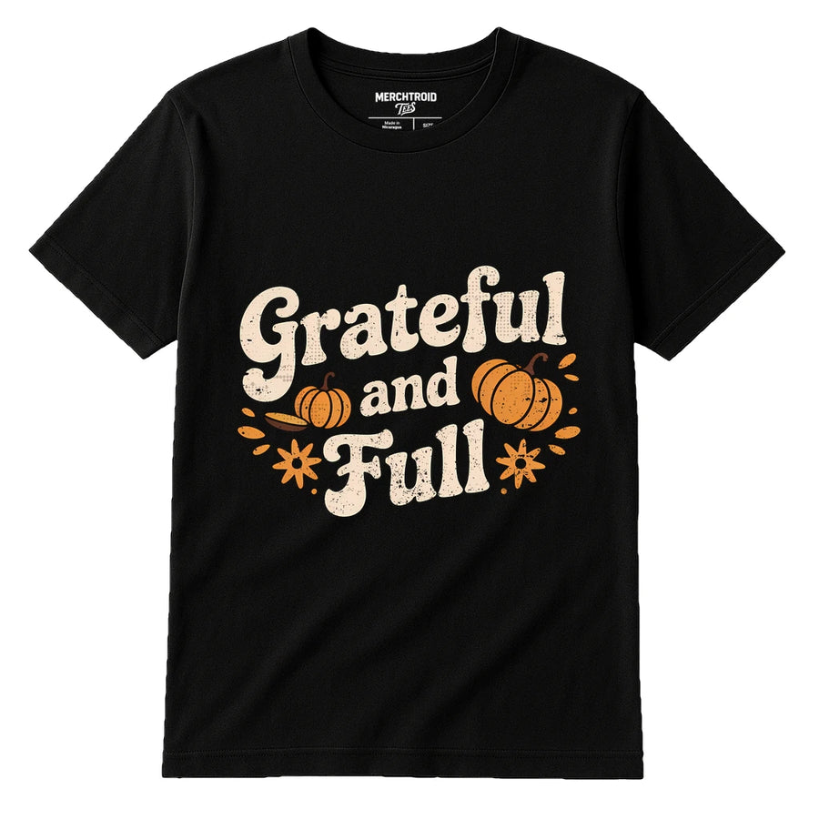 A black t-shirt with the text "Grateful and Full" in a vintage-style font. The design includes decorative orange pumpkins and floral elements surrounding the text.