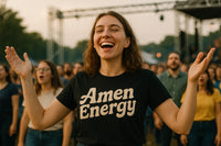 A person with shoulder-length brown hair is smiling broadly with arms raised, wearing a black T-shirt that says 