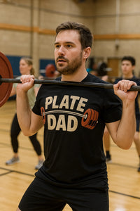A person with short hair and a beard, wearing a black t-shirt with the text 
