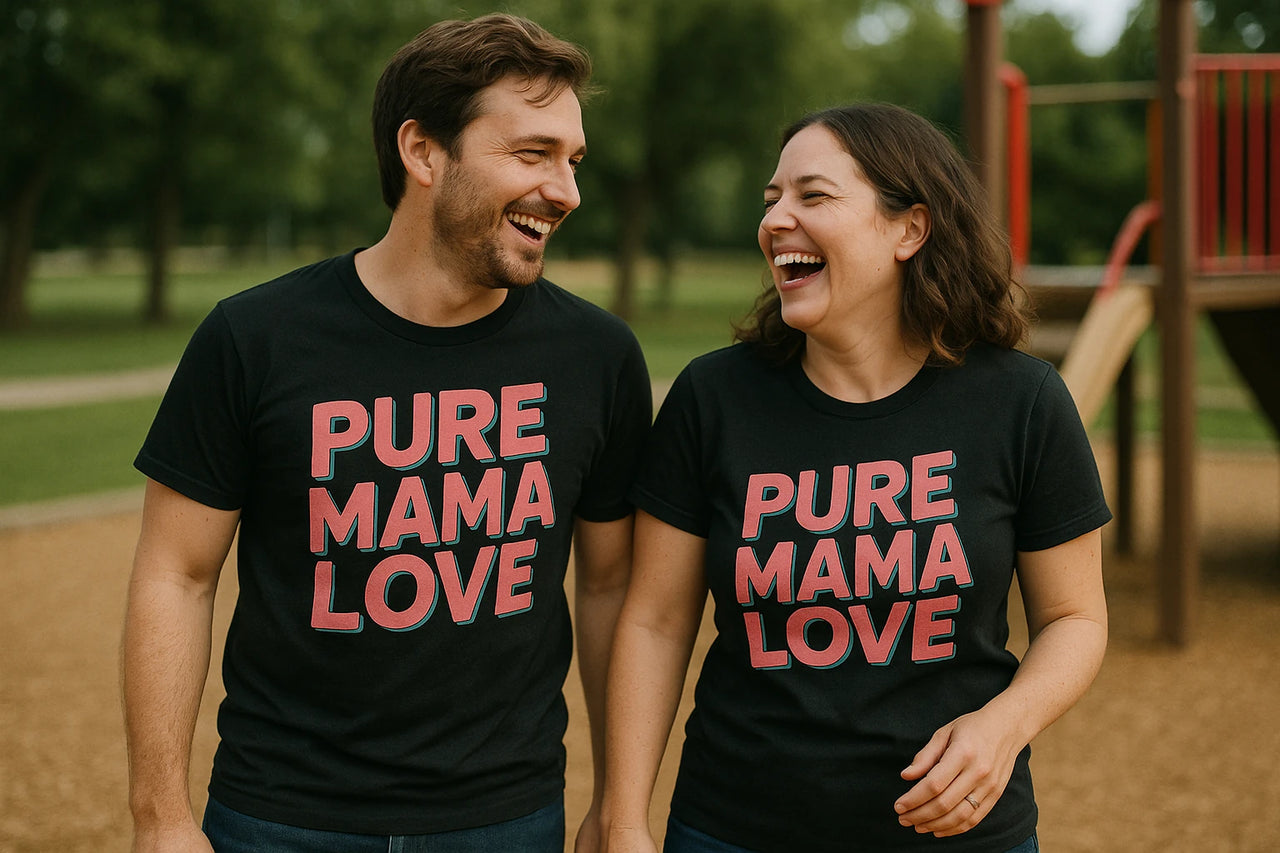 A man and a woman are laughing together at a park. They are both wearing matching black T-shirts with the text "PURE MAMA LOVE" printed in bold letters. They appear happy and are walking side by side, with playground equipment visible in the background.