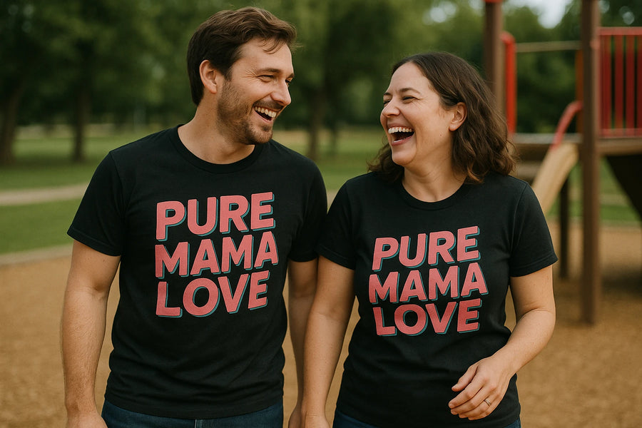 A man and a woman are laughing together at a park. They are both wearing matching black T-shirts with the text "PURE MAMA LOVE" printed in bold letters. They appear happy and are walking side by side, with playground equipment visible in the background.