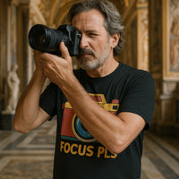A bearded man with gray hair is wearing a black T-shirt with a colorful camera graphic and the text 