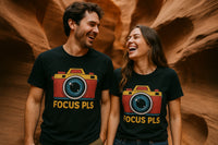A man and woman are laughing and looking at each other, wearing matching black t-shirts with a colorful camera graphic and the words 