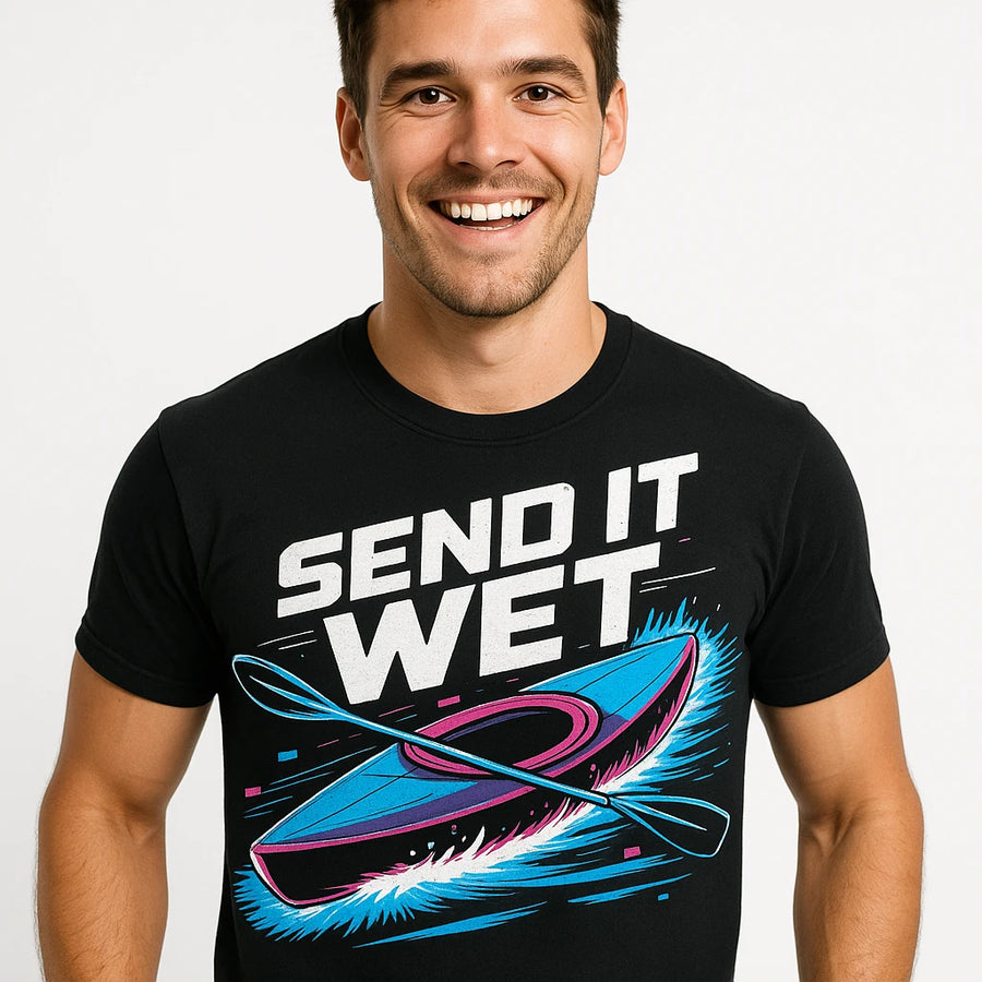 A person with short dark hair wearing a black T-shirt with the text "SEND IT WET" in bold white letters. The design includes an illustration of a kayak and paddles in vibrant blue and pink colors. The person is smiling against a plain white background.