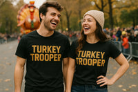 Two people are standing outdoors at what appears to be a parade. They are both wearing black shirts with the phrase 