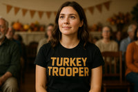 A person with long brown hair is seated in a room with festive autumn decorations in the background. They are wearing a black shirt with the words 