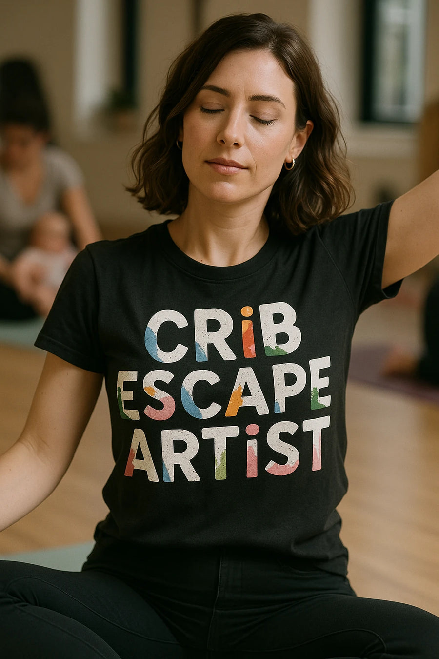 A person with shoulder-length brown hair and closed eyes wearing a black t-shirt that says "CRIB ESCAPE ARTIST" in colorful, bold letters. They appear to be in a calm, seated position, possibly meditating or focusing, in a room with others in the background.