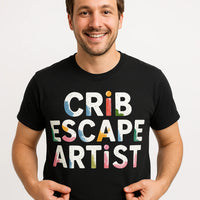 A person wearing a black T-shirt with colorful text. They are smiling and holding the sides of the shirt with their hands.