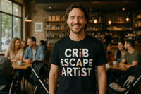 A person is smiling and standing in a cozy café environment. They are wearing a black t-shirt with the text 