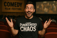 A person is in a theater with red seats, smiling widely and holding their hands up in a playful gesture. They are wearing a black T-shirt with the text 