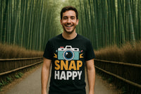 A person smiling widely while standing in a bamboo forest. They are wearing a black t-shirt with a graphic of a camera and the text 