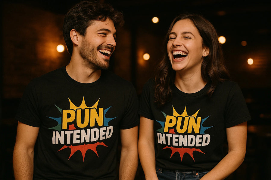 A man and a woman are standing side by side, both laughing heartily. They are wearing matching black T-shirts featuring the text "PUN INTENDED" in bold letters with colorful comic-style bursts behind the words. The background is softly lit with blurred warm lights, creating a cozy atmosphere.