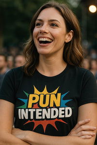 A person with shoulder-length brown hair is smiling broadly. They are wearing a black shirt with colorful text reading 