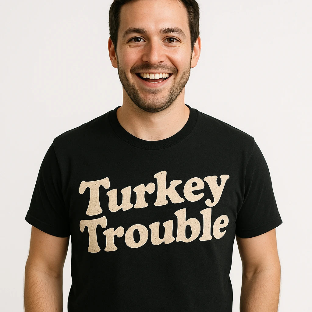 A person is smiling and wearing a black T-shirt with the text "Turkey Trouble" printed on it. The background is plain white.