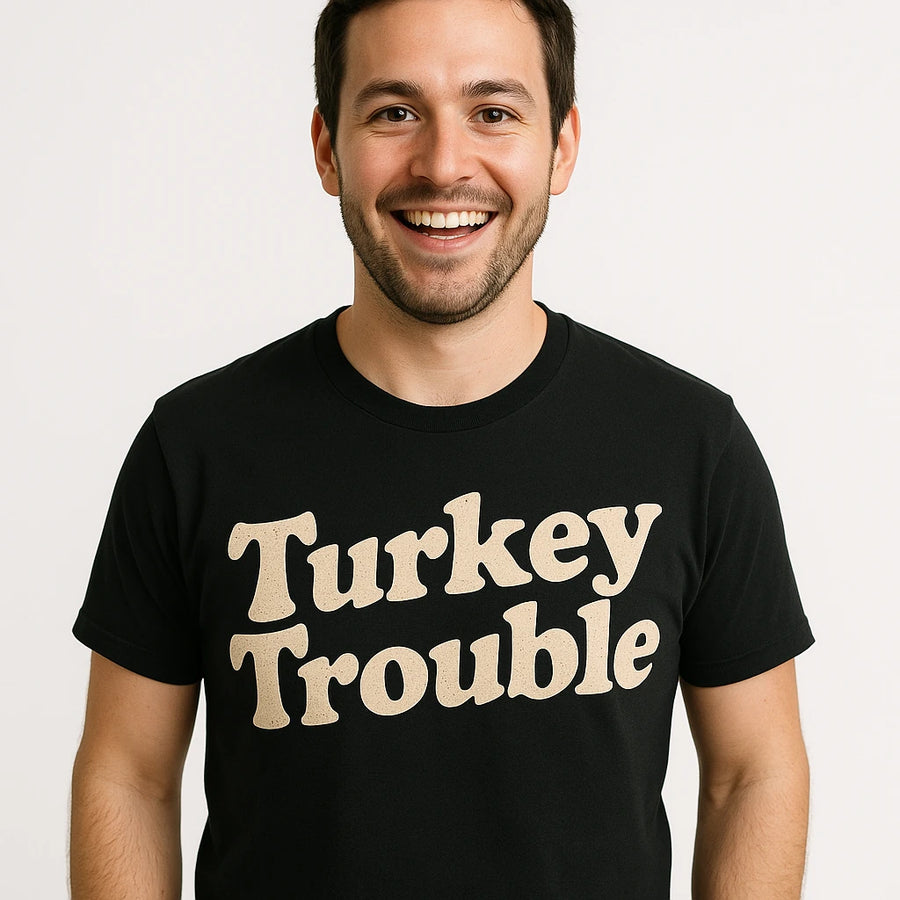 A person is smiling and wearing a black T-shirt with the text "Turkey Trouble" printed on it. The background is plain white.